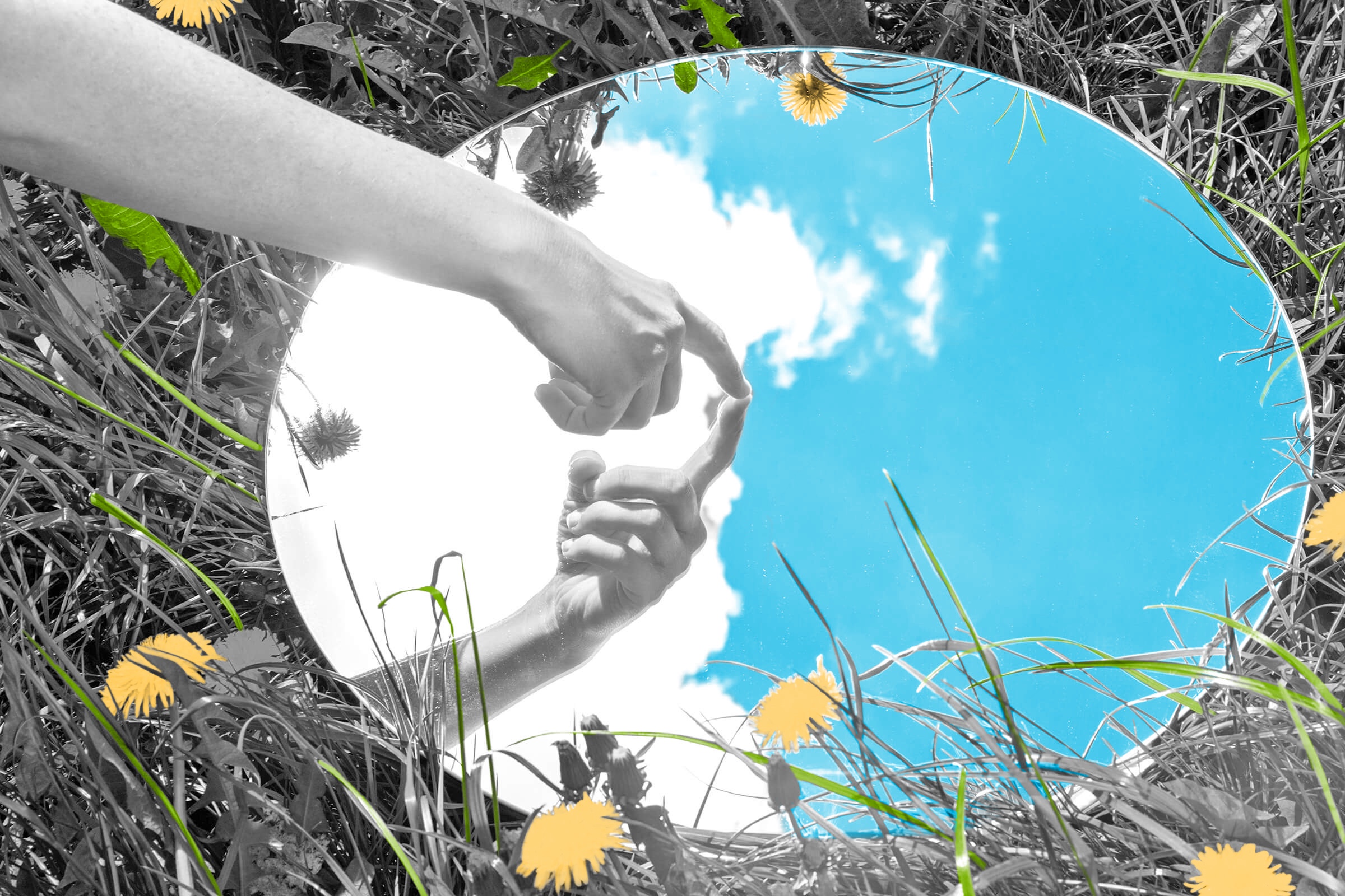 Hand pointing to its own reflection in a mirror laid in the grass